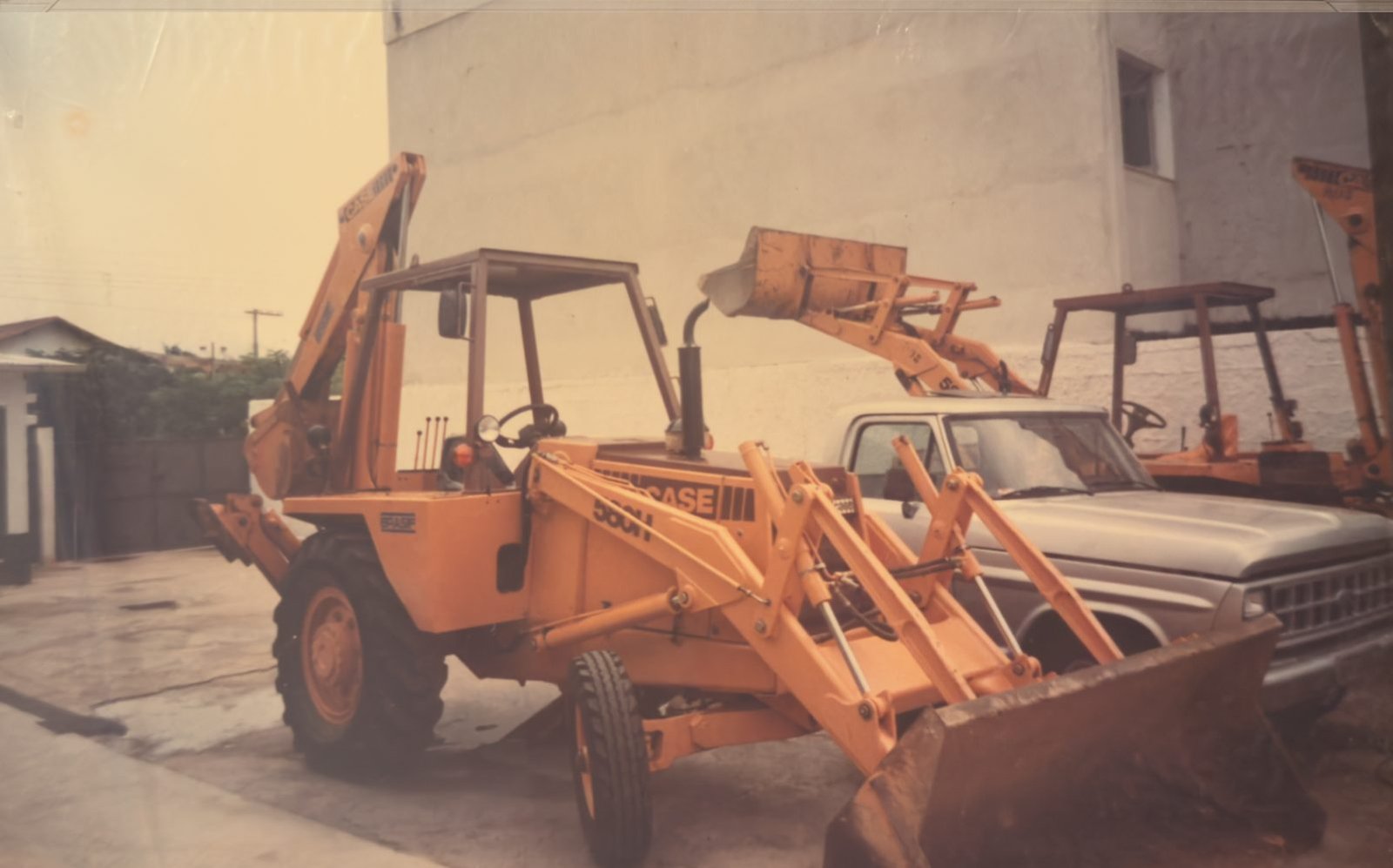 Fotografia antiga de uma retroescavadeira CASE 580H ao lado de uma caminhonete, nos primeiros anos da Escave